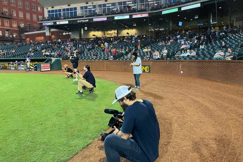 University Communications photographers and videographers working at a Greensboro Grasshoppers baseball game.