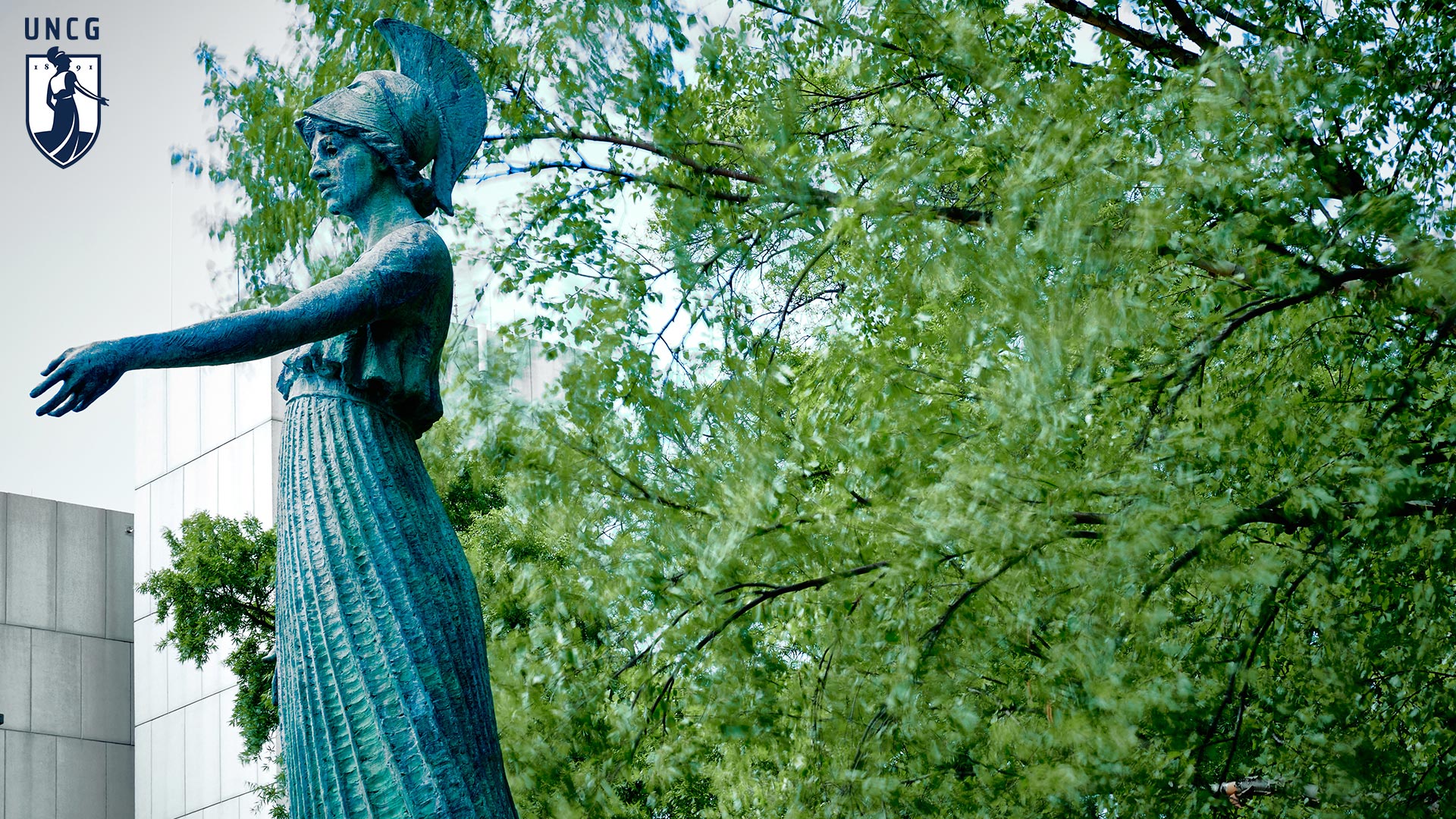Minerva statue on the left showing a tree in the background with the UNCG logo in the top left corner