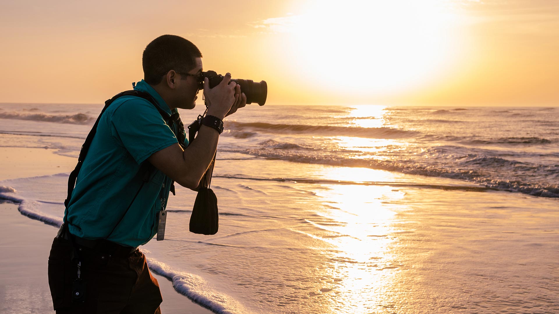 A male photographer taking a photo of the surf at the ocean,