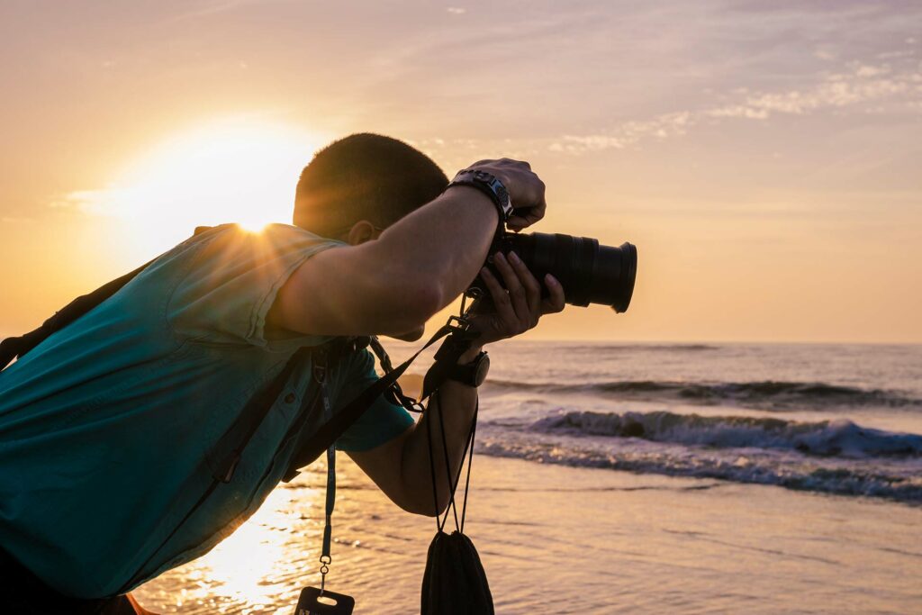 Photographer with camera taking picture of ocean at sunset.