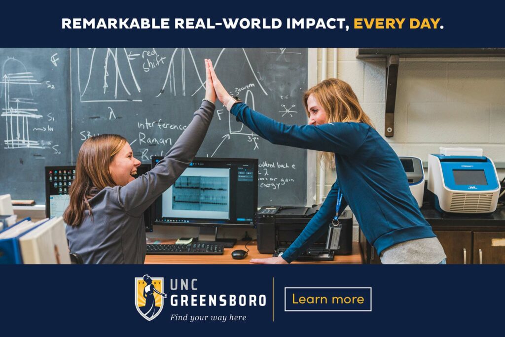 Ad design showing UNCG branding over photo of two women doing a high five at a computer workstation.