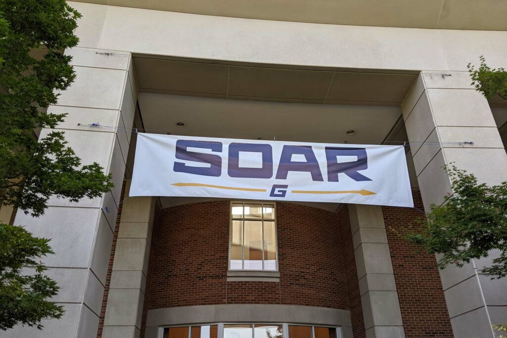 A UNCG banner sign for SOAR hanging over a building entrance way